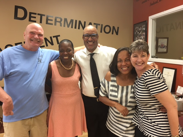 two men and three women smiling and standing with arms around each other
